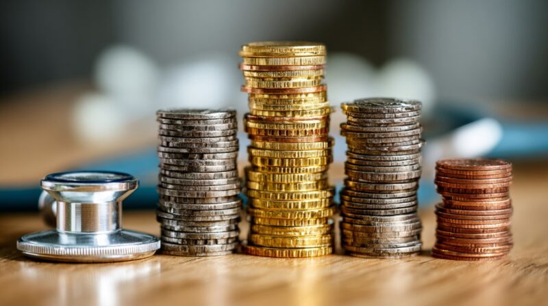 Stacks of coins beside a stethoscope symbolizing healthcare costs