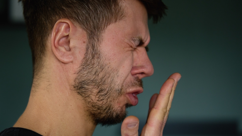A man reacts to his own bad breath, suggesting it might be linked to digestive problems
