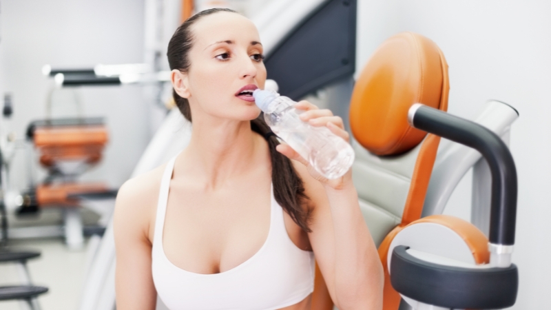 A woman drinks water after a workout to rehydrate and prevent stomach upset after exercising