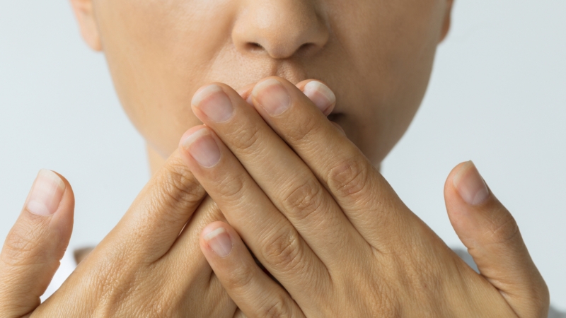 A woman covers her mouth with both hands, showing concern about persistent bad breath possibly linked to stomach issues