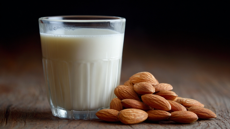 A glass of almond milk placed beside a small pile of whole almonds on a wooden surface