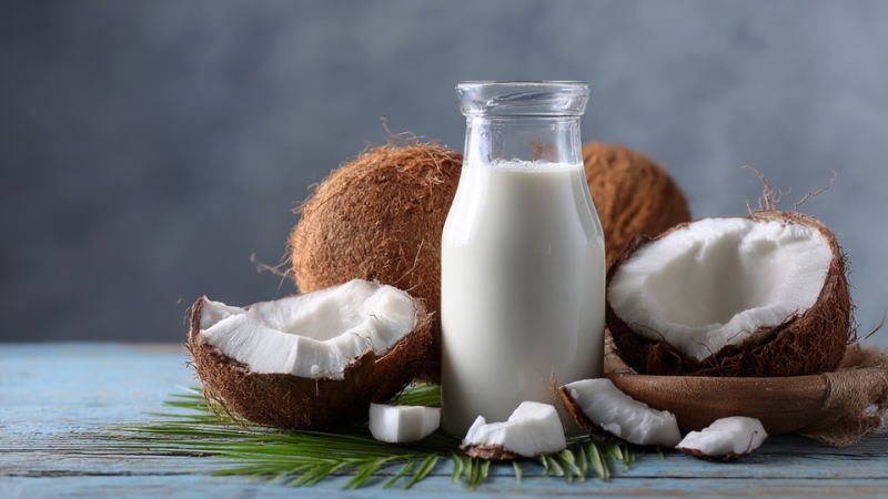 A bottle of coconut milk surrounded by whole coconuts and fresh coconut pieces