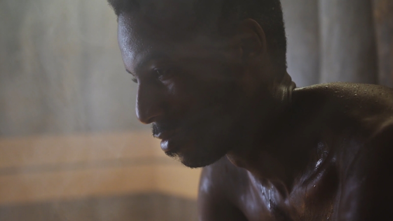 A man sits in hot steam with sweat on his skin during a heat session