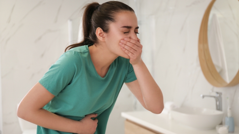 Woman covers mouth and holds stomach, showing acid reflux symptoms with vomiting