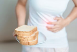 Person holding bread and pressing stomach due to bloating after eating