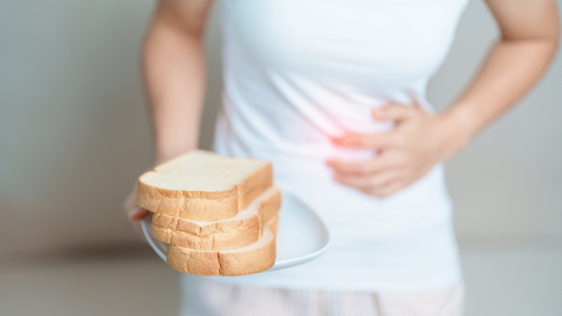 Person holding bread and pressing stomach due to bloating after eating