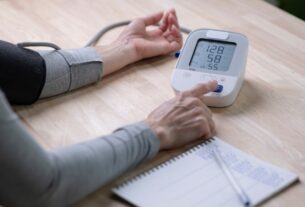 Person checking blood pressure at home with a digital monitor showing a 128/58 reading