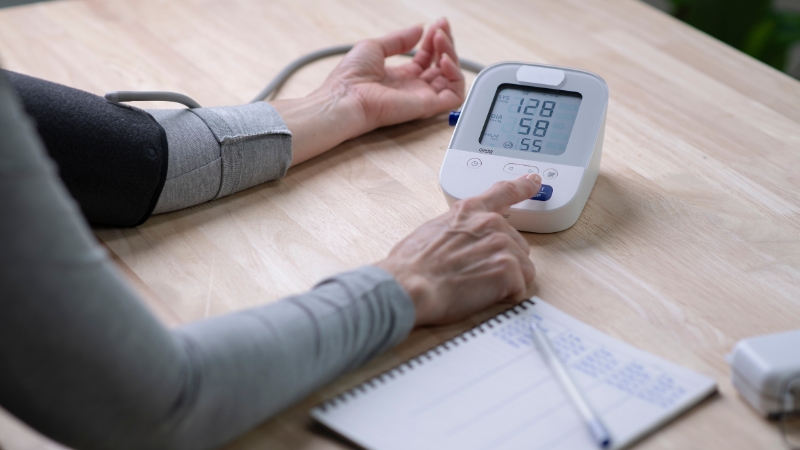 Person checking blood pressure at home with a digital monitor showing a 128/58 reading