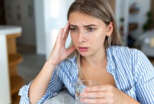 Woman holding a glass of water while experiencing headache and dizziness symptoms