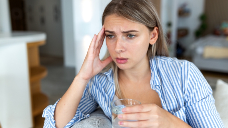 Woman holding a glass of water while experiencing headache and dizziness symptoms