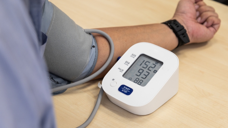 Digital blood pressure monitor showing a 152/93 reading on a person’s arm