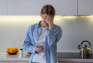 Woman holding a glass of water with a headache, showing early signs of dehydration in adults
