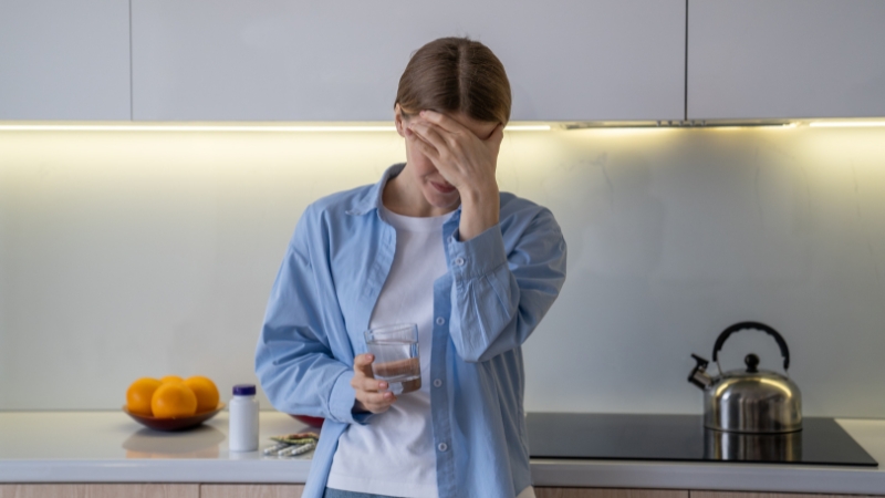 Woman holding a glass of water with a headache, showing early signs of dehydration in adults
