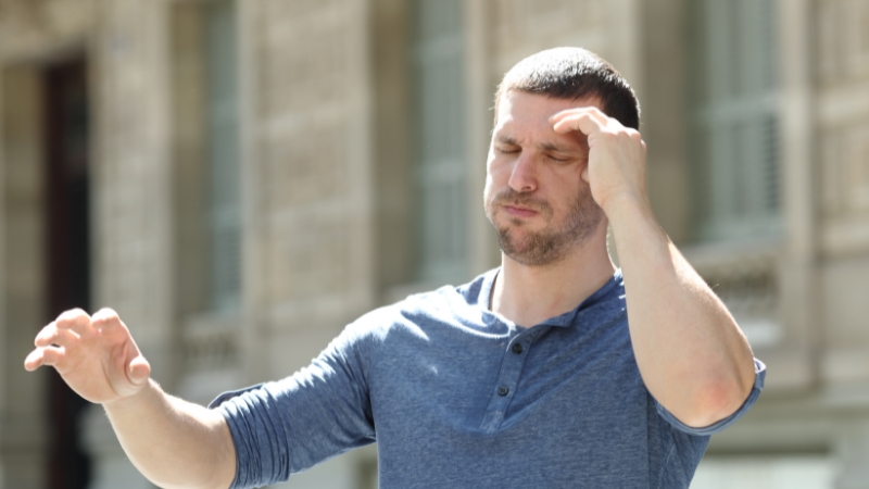 Man holding his head and feeling dizzy outdoors