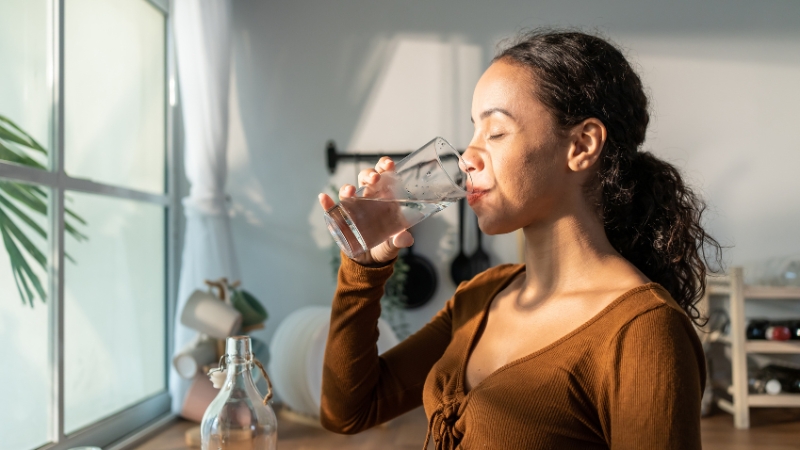 Woman drinking a glass of water at home in natural light