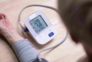 Digital blood pressure monitor on a table connected to a cuff on a person’s arm