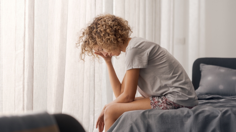 Woman sitting on bed with her head down, showing morning fatigue and low energy