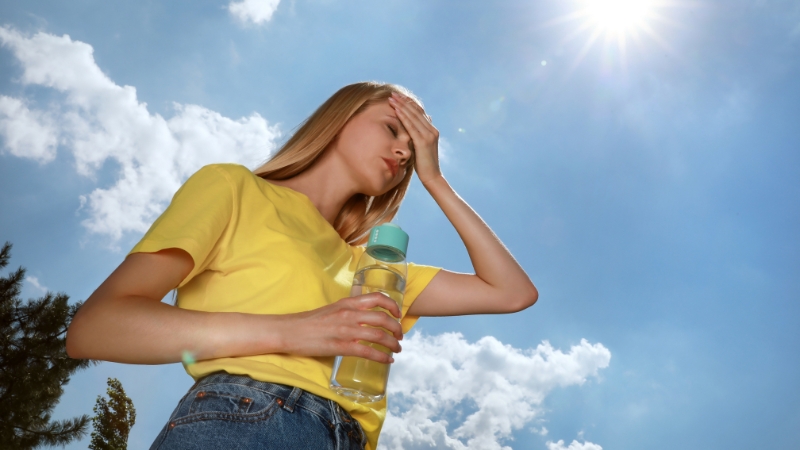 Woman holding a water bottle under the sun, showing dehydration signs