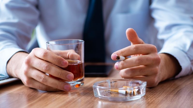 Person holding a cigarette and a glass of alcohol, showing habits that can worsen dry mouth