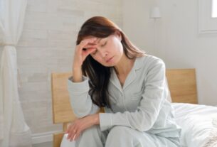 Woman sitting on bed holding her head, showing signs of waking up tired every morning
