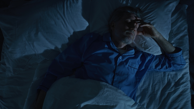 Man lying awake in bed at night, showing poor sleep quality and waking up tired