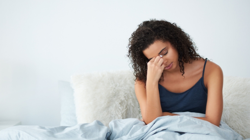 Woman sitting in bed looking exhausted and holding her forehead after waking up tired