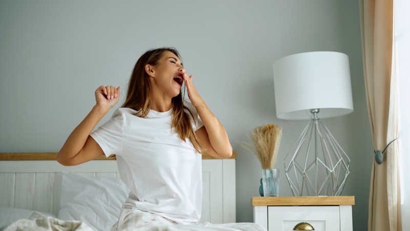 Woman yawning in bed in the morning, showing signs of waking up tired