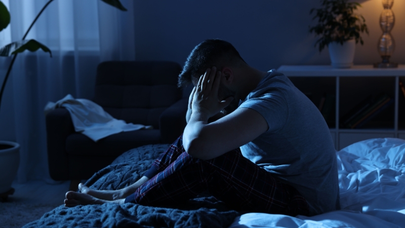 Man sitting awake at night struggling with a disrupted sleep schedule