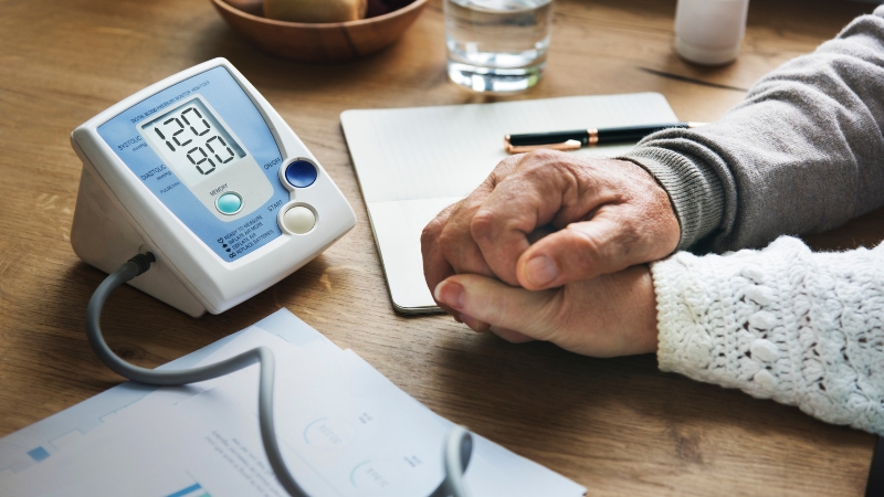 Blood pressure monitor on a desk showing a 120/80 reading next to a person’s hands