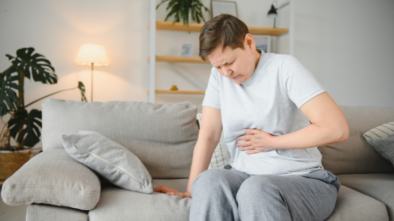 Person sitting on a couch holding stomach due to persistent bloating and discomfort