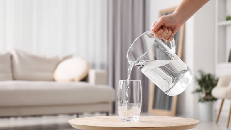 Hand pouring water into a glass from a pitcher indoors