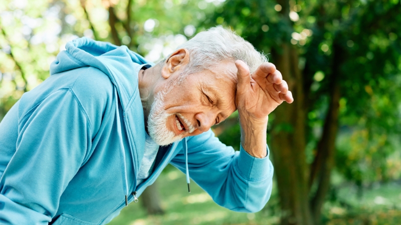 Older man holding his head outdoors, showing dehydration symptoms